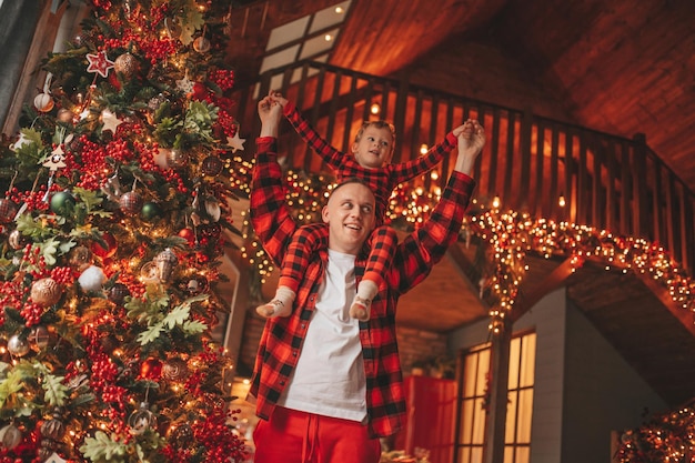 Candid authentic happy dad and son in red plaid pajamas fooling around at wood lodge Xmas decorated