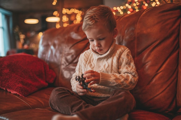 Candid authentic happy little boy in knitted beige sweater fooling around at lodge Xmas decorated