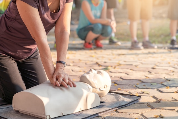 Candid of mature asian female or older runner woman training on CPR demonstrating class in outdoor park and put hands over CPR doll on chest. First aid training for heart attack people or lifesaver.