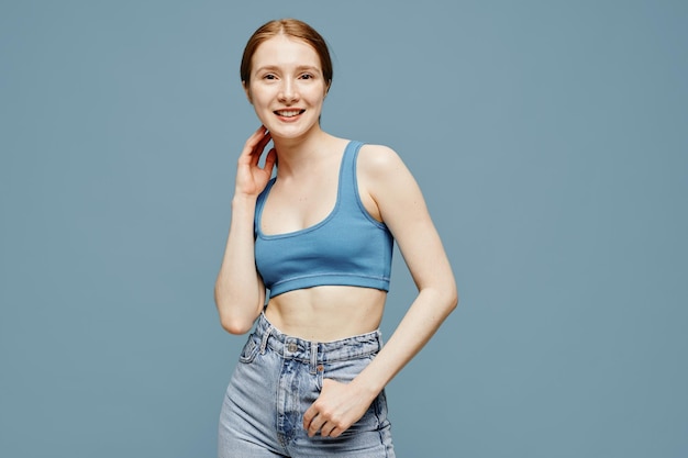 Candid portrait of fair skinned young woman with red hair smiling at camera while posing against pas