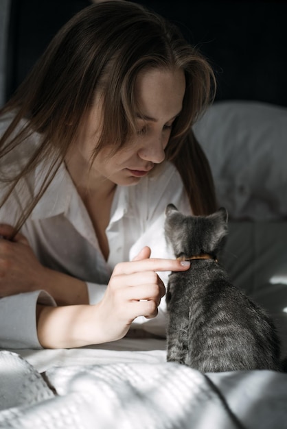 Candid portrait of young woman is resting with kitten pet on the bed at home one sunny day