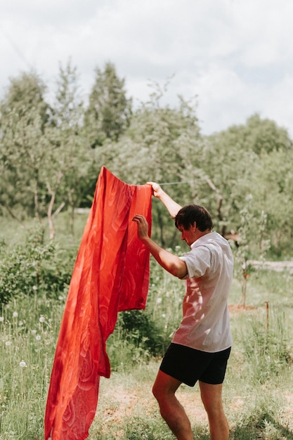 Candid young mature choring man chore homework and hanging the laundry to dry on a clothesline on the street in courtyard of village household cottage house summer freshness and laundry day