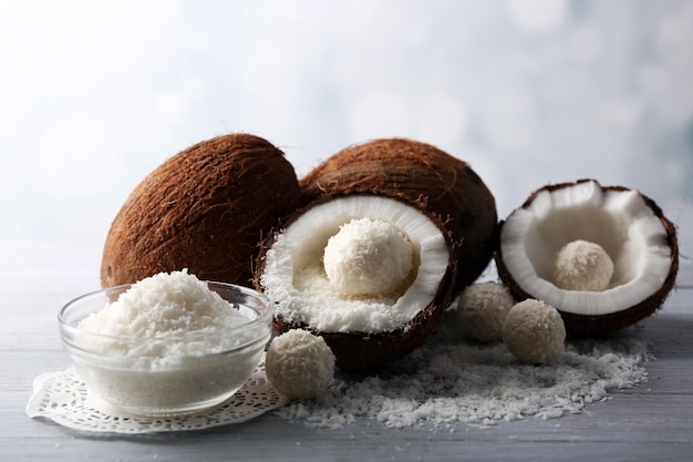 Candies in coconut flakes and fresh coconut on color wooden background