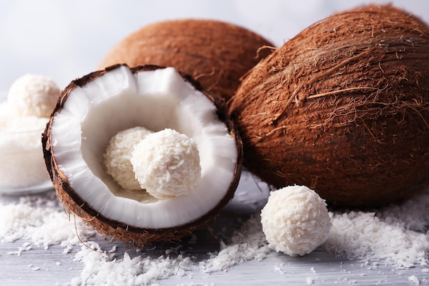 Candies in coconut flakes and fresh coconut on color wooden background