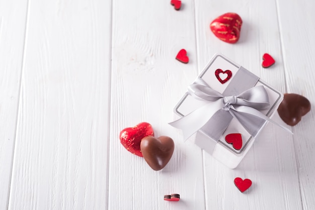 Candies hearts and gift box on wooden board