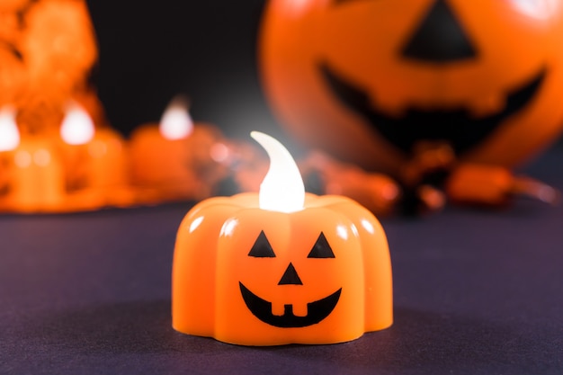 A candle in the form of a pumpkin glows against a dark background.