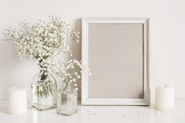 Candles, gypsophila flowers and photo frame on table wall background. Front view mockup.