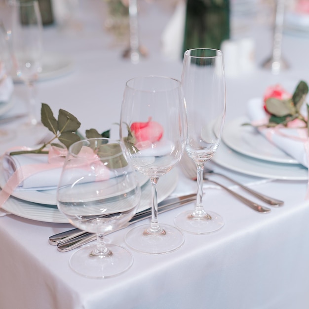 Candles and vase with white roses placed on round table near wineglasses during romantic date in garden