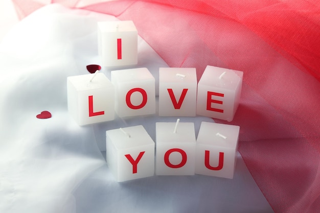 Candles with printed sign I LOVE YOU, on white fabric background