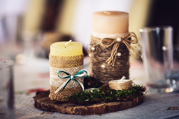 Candles wrapped in burlap and decorated with a bow-knot, lace and moss on a wooden stand.