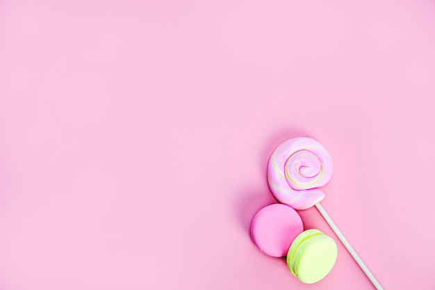 Candy sweets concept pink lollypop and donuts macarons on pink background copy space top view