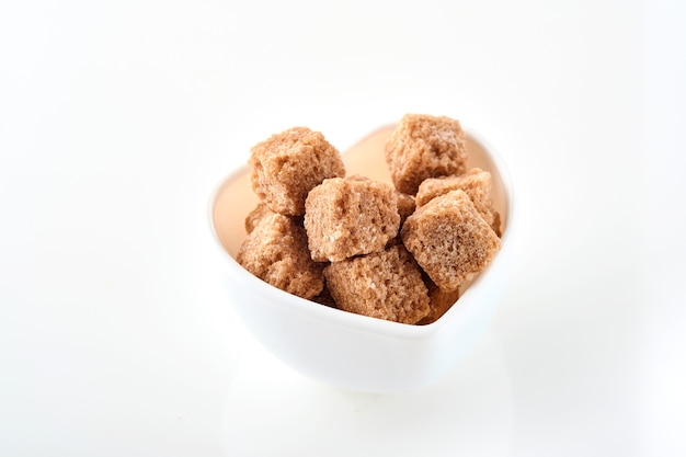 Cane sugar cubes in a white bowl isolated on white background. Selective focus.