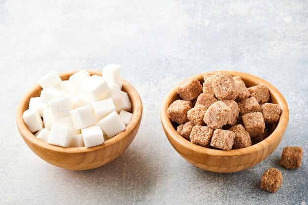 Cane sugar and white sugar cube in bamboo bowl on gray table concrete