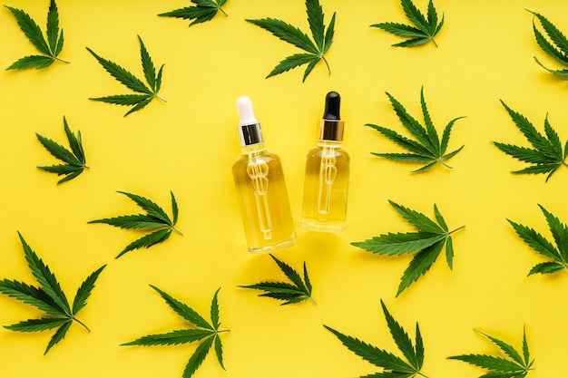 Cannabis leaf pattern with cosmetic product CBD oil on yellow background with copy space.