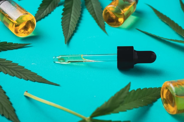 Photo cannabis oil in dropper bottles with green leaves on green background alternative medicine concept