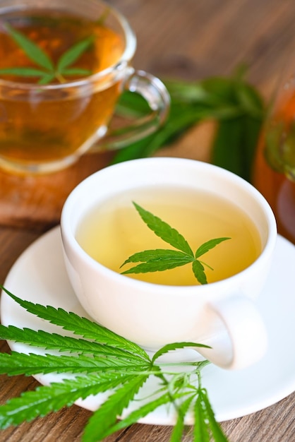 Cannabis tea herbal on tea cup with cannabis leaf marijuana leaves herb on wooden background health tea with hemp leaf plant THC CBD herbs food and medical concept