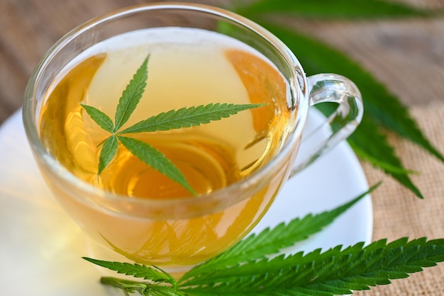 Cannabis tea herbal on tea cup with cannabis leaf marijuana leaves herb on wooden background, health tea with hemp leaf plant THC CBD herbs food and medical concept