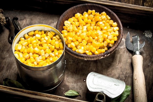 Canned corn in a tin can with opener. On a wooden background.