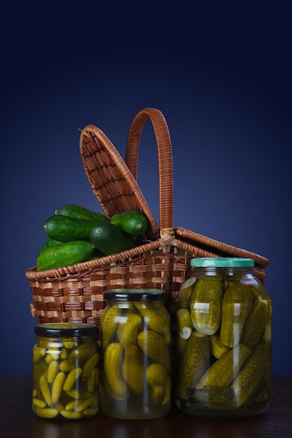 Canned cucumbers in jars and a basket of fresh cucumbers.