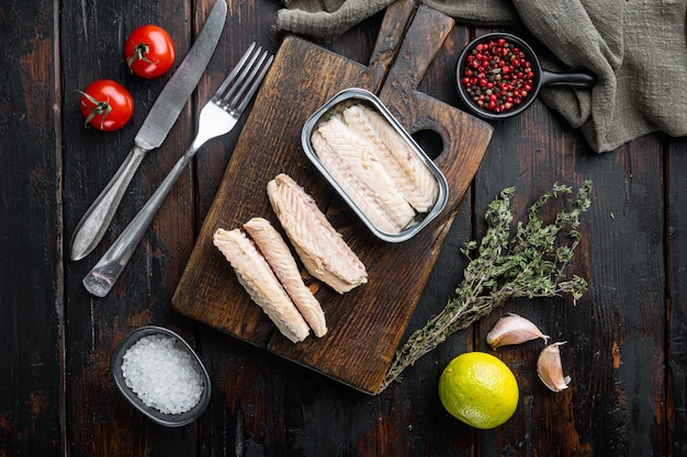 Canned Mackerel fillet, fish preserves, on wooden cutting board, on old dark wooden table
 with herbs and ingredients, top view flat lay