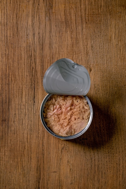 Photo canned tuna fish in oil in opened can over wooden background. top view, copy space