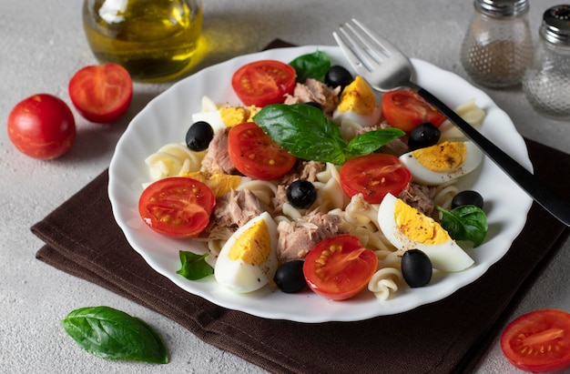 Canned tuna salad with pasta cherry tomatoes black olives boiled egg and basil Closeup