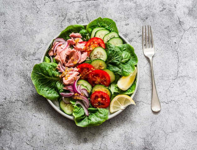 Canned tuna tomatoes cucumbers romaine salad red onion olive oil salad delicious healthy food on a grey background top view