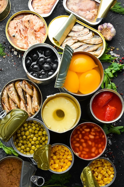 Canned vegetables beans fish and fruits in tin cans on black stone background Food stocks