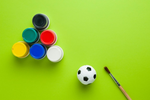 cans of paint lie in the shape of a triangle next to a brush and a mini soccer ball