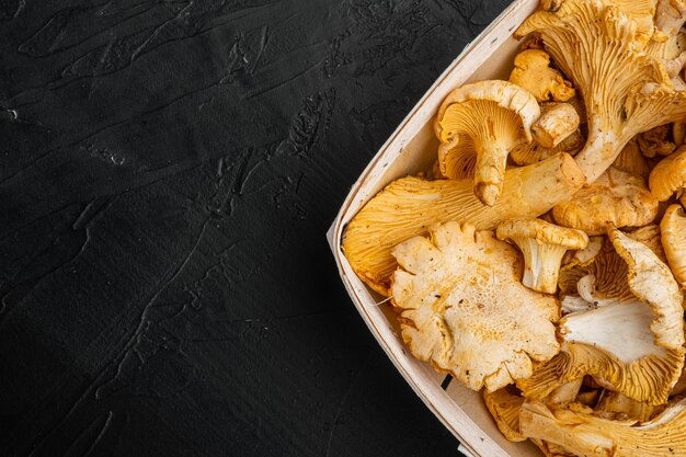 Cantharellus cibarius commonly known as the chanterelle set in wooden box container on black dark stone table background top view flat lay with copy space for text