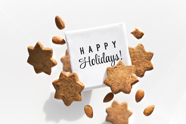 Canvas with text Happy Holidays flying levitating with star cookies almonds Group of tasty snacks around text board Isolated on white Creative food arrangement greeting card design