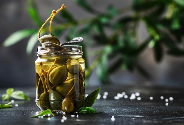 Capers Marinated or pickled canned capers fruit close up in glass jar on gray kitchen table background Copy space