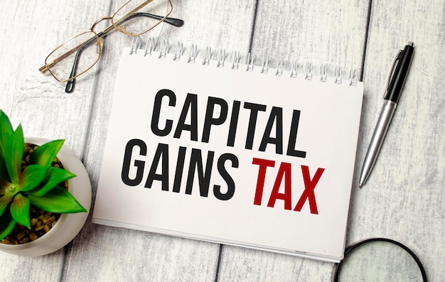 Capital gains tax words on notebook and pen glasses and magnifier