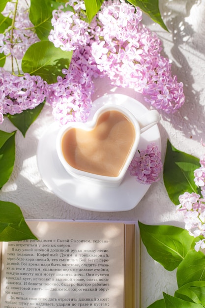 Cappuccino coffee in a cup and a branch of lilac on a white background with shadows