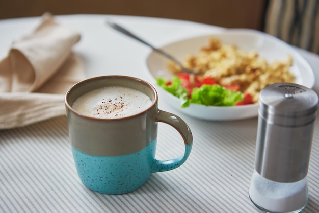 Cappuccino coffee in cup and plate with scrambled eggs and tomatoes breakfast on the table