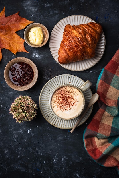 Cappuccino coffee with croissant on the table, autumn breakfast concept, top view