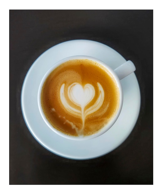 Cappuccino coffee, with flower pattern, white cup and black background.