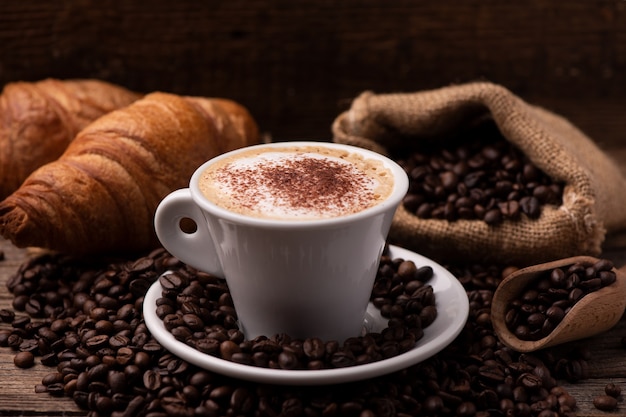 Cappuccino and croissant with coffee beans close up