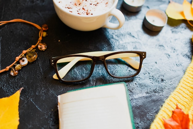 Cappuccino, glasses and a bright yellow sweater lie on dark 