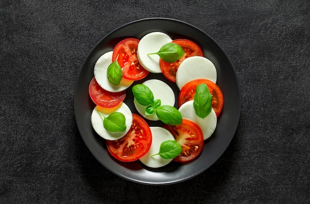 Caprese Italian appetizer on plate on dark background top view space to copy text