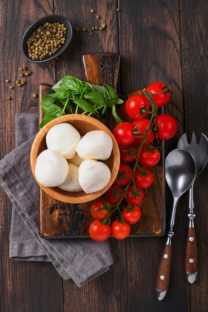 Caprese salad ingredients for cooking Cutting wooden board with traditional caprese preparation ingridients mozzarella tomatoes basil olive oil cheese spices on wooden rustic background