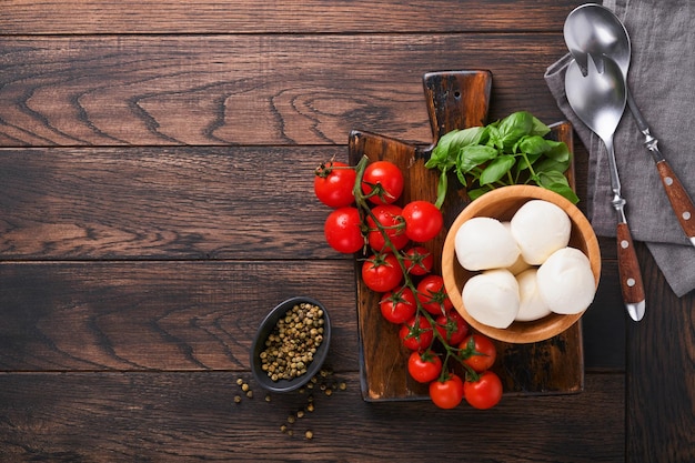 Caprese salad ingredients for cooking Cutting wooden board with traditional caprese preparation ingridients mozzarella tomatoes basil olive oil cheese spices on wooden rustic background