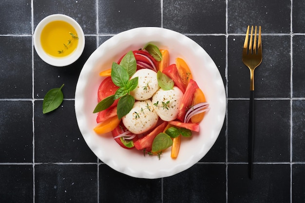 Caprese salad Italian caprese salad with sliced tomatoes mozzarella cheese basil olive oil in white plate over old brick tiles black background Delicious Italian food Top view Rustic style