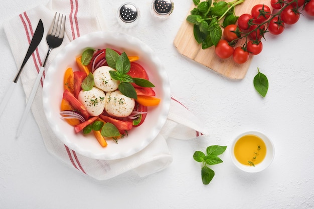 Caprese salad Italian caprese salad with sliced tomatoes mozzarella cheese basil olive oil in white plate over white background Delicious Italian food Top view Rustic style