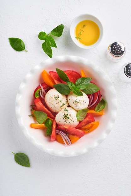 Caprese salad Italian caprese salad with sliced tomatoes mozzarella cheese basil olive oil in white plate over white background Delicious Italian food Top view Rustic style