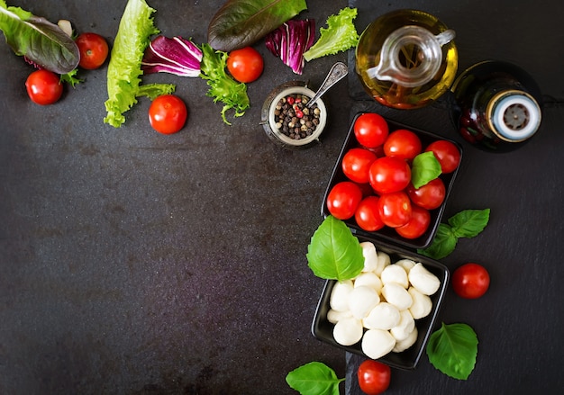 Caprese salad tomato and mozzarella with basil and herbs oon black background. Top view