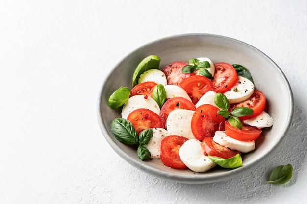 Caprese salad with tomatoes mozzarella basil and olive oil with a basil leaf near on white background Text space