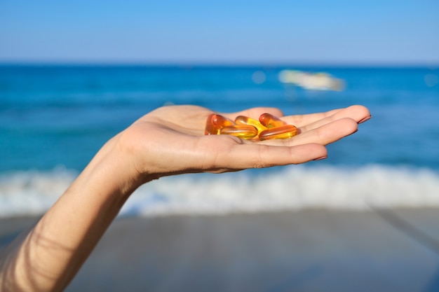 Capsule of vitamin d, e, a, omega 3, fish oil in the hand close-up. Blue sea, sky background. Healthy eating, medicine, lifestyle, nutritional supplements concept