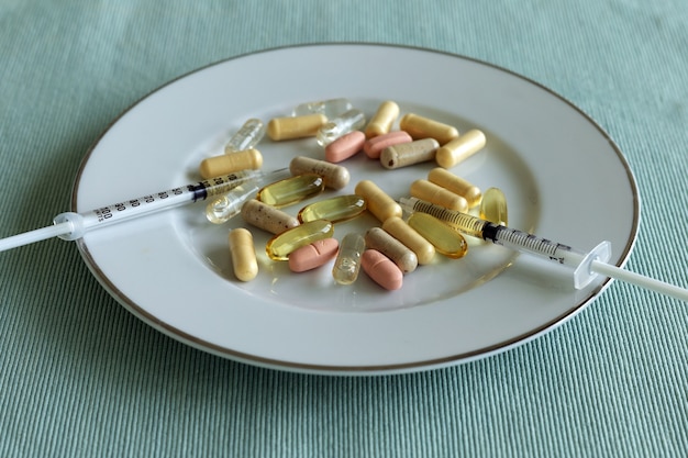 Capsules pills and syringes on the plate on a table. Medicine as a food concept.