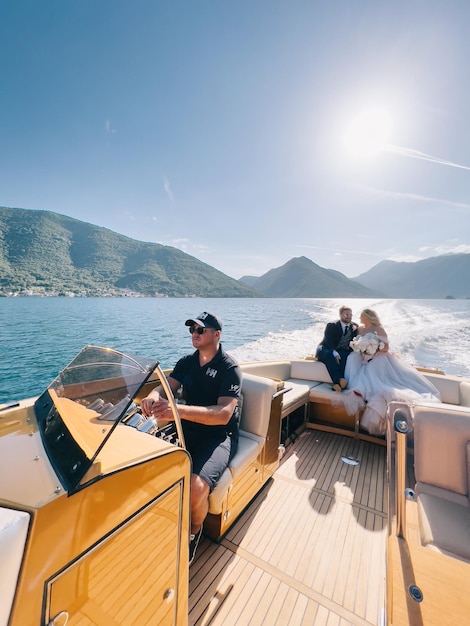 Captain sits at the helm of the yacht with the bride and groom on board floating on the sea